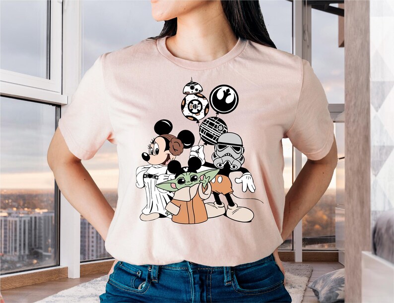 May include: A pink t-shirt with a graphic print of Mickey Mouse, Yoda, and a Stormtrooper holding balloons. The balloons are shaped like the Death Star, a TIE fighter, and a BB-8 droid.