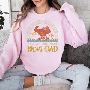 a woman sitting on a couch wearing a pink sweatshirt