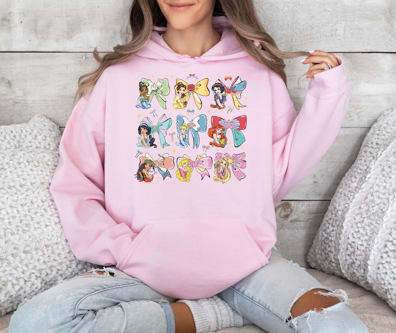 a woman sitting on a bed wearing a pink hoodie