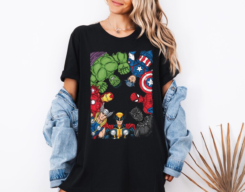 A woman wearing a black t-shirt with a graphic of various Marvel superheroes, including Hulk, Captain America, Spider-Man, and others, standing against a white background.