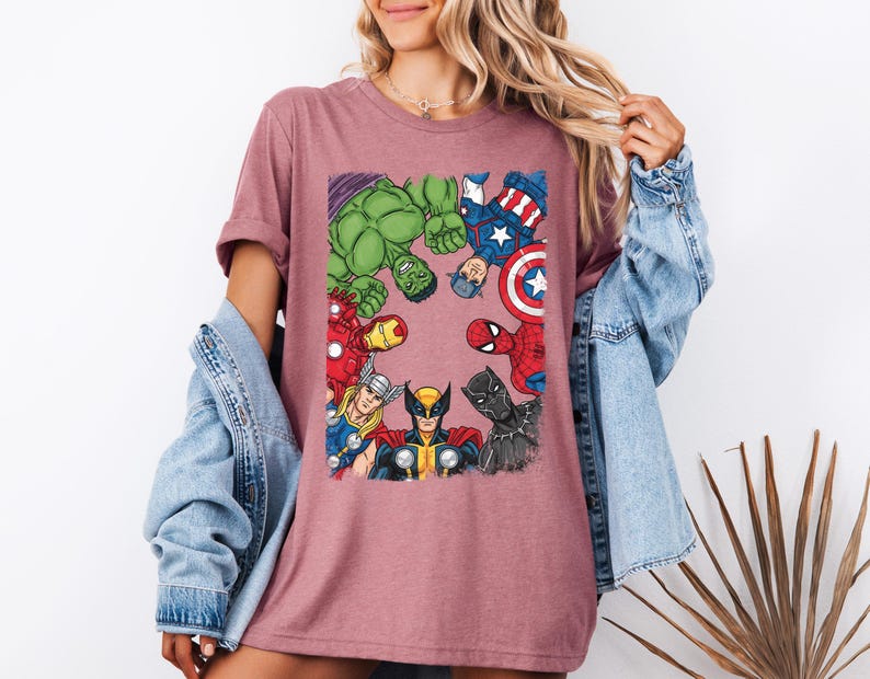 A woman wearing a pink t-shirt with a graphic of various Marvel superheroes, including Hulk, Captain America, Spider-Man, and others, standing together.