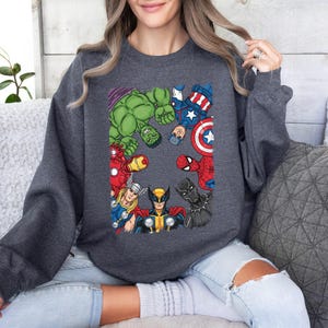A woman wearing a gray sweatshirt with a graphic of various Marvel superheroes, including Hulk, Captain America, Spider-Man, and others, arranged in a circular pattern.