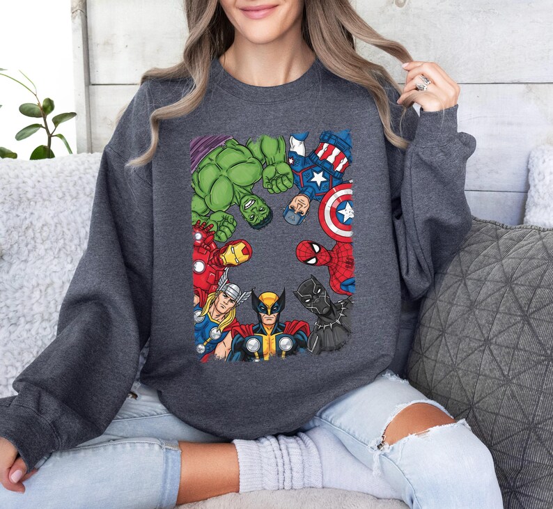 A woman wearing a gray sweatshirt with a graphic of various Marvel superheroes, including Hulk, Captain America, Spider-Man, and others, arranged in a circular pattern.