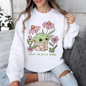 a woman sitting on a couch wearing a sweatshirt with a baby yoda on it