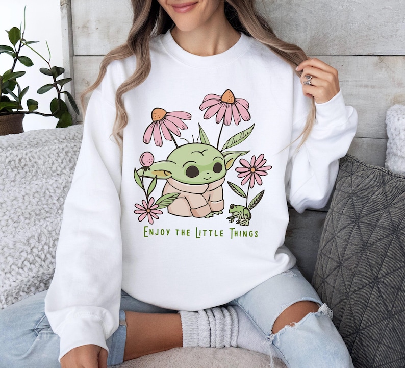 a woman sitting on a couch wearing a sweatshirt with a baby yoda on it