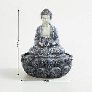 May include: A gray Buddha statue, 25 cm tall and 19 cm wide, seated in a lotus position, holding a lotus flower. The statue is atop a lotus-shaped base, creating a serene and spiritual ambiance. Ideal for home decor.