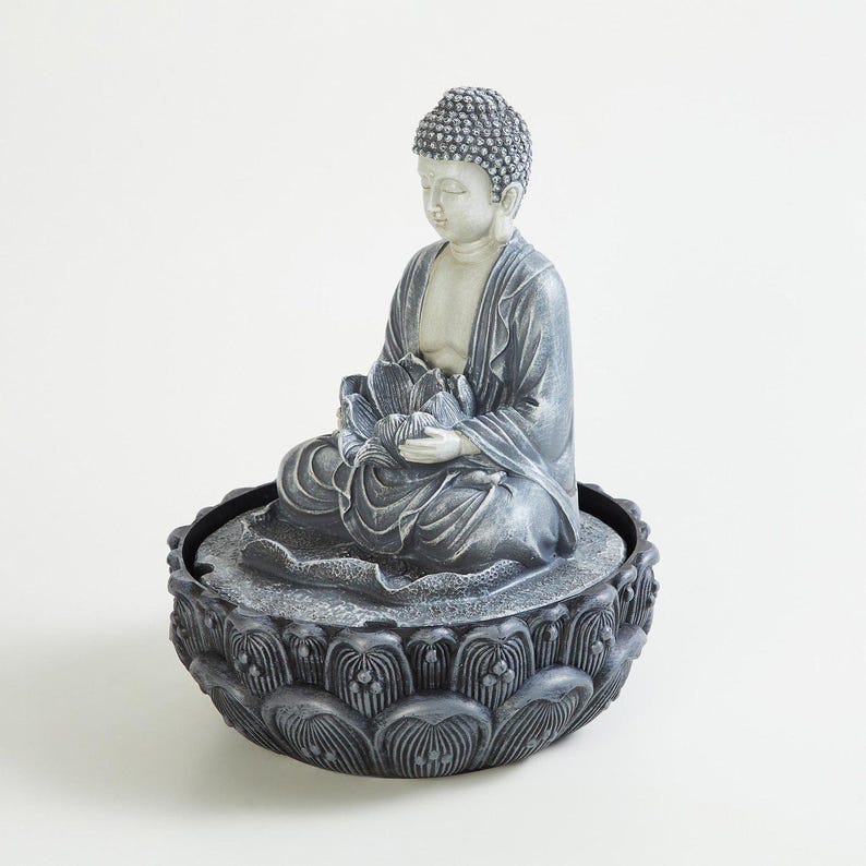 May include: A gray Buddha statue seated in a meditative pose, holding a lotus flower. The statue is on a decorative, dark gray lotus-shaped base. The Buddha's robe is a muted gray, and the overall design is serene.
