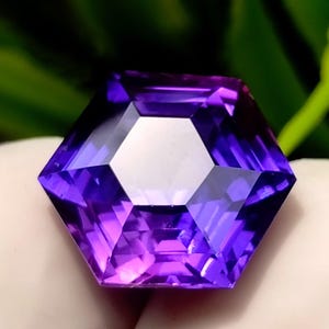 Può includere: Una gemma esagonale sfaccettata, con una faccetta centrale bianca e sfumature viola. Le sfaccettature della gemma riflettono la luce, creando un effetto scintillante. La gemma è presentata su uno sfondo sfocato verde e bianco.