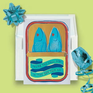 May include: Greeting card with a sardine can design. The can features two blue fish with red hearts, and the text "You're the only fish in the sea for me." The card is inside a white envelope, with blue ribbon and a bow.