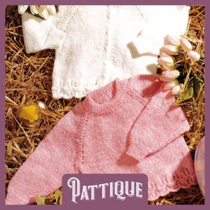 Könnte beinhalten: Zwei gestrickte Baby-Pullover, einer weiß und einer rosa, auf einem Strohboden ausgelegt. Die Pullover haben eine zarte Spitzenborte und sind perfekt für ein Neugeborenes.