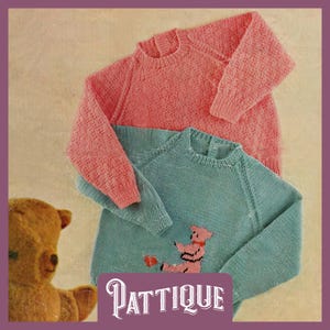 May include: Two knitted sweaters, one pink and one teal blue. The teal blue sweater has a pink bear applique on the front. The sweaters are laid out on a light brown surface.