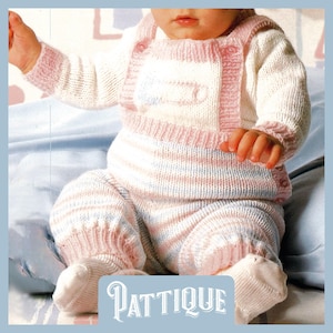 May include: A baby in a knitted outfit, featuring a white top and striped pink and blue trousers. The outfit has pink edging and a safety pin design. The word "PATTIQUE" is printed at the bottom.