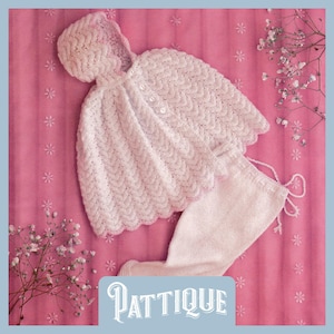 Op de afbeelding: Een witte, gehaakte babyoutfit, bestaande uit een capuchoncape en een broek met trekkoord, wordt getoond op een roze achtergrond. De cape heeft een geschulpte rand en een knoopsluiting. De tekst "PATTIQUE" staat onderaan.
