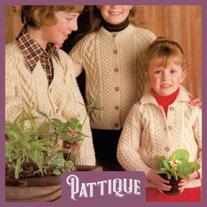 May include: Three children wearing cream colored cable knit cardigans with button closures. The cardigan on the left has a v-neck. The cardigan in the middle has a round neck. The cardigan on the right has a collar. The children are standing in front of a wooden background.