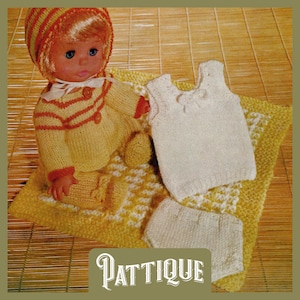 May include: A knitted doll outfit set in yellow and white. The set includes a hat, sweater, vest, and trousers. The doll is wearing the outfit and is sitting on a yellow and white knitted blanket.