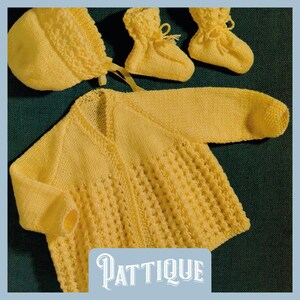 Puede incluir: Un conjunto de punto amarillo para bebé compuesto por un cárdigan, un gorro y unas botitas. El cárdigan tiene cuello en V y cierre de botón. El gorro tiene un borde festoneado. Las botitas tienen una punta puntiaguda y un lazo de cinta.