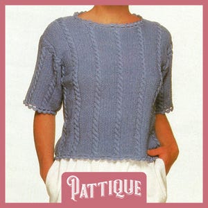 May include: A light blue knitted jumper with a cable knit pattern and a scalloped neckline and sleeves. The jumper is cropped and has a relaxed fit.