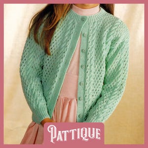 May include: A light green knitted cardigan with a cable knit pattern and button closure. The cardigan is worn over a pink dress.