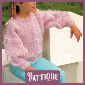 May include: A pink knitted cardigan with pearl buttons and white bows on the sleeves. The cardigan is made of a soft, fluffy yarn.