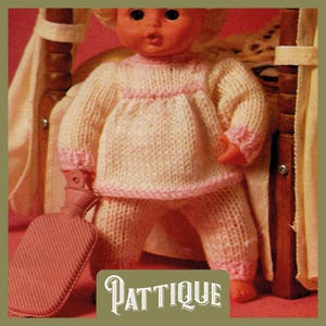 May include: A knitted doll outfit in pink and white with a pink trim. The outfit is a long-sleeved shirt and pants. The doll is holding a red hot water bottle.