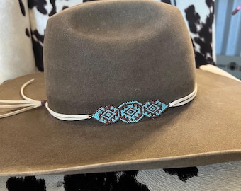 May include: A brown felt hat with a decorative beaded band. The band features a geometric pattern in turquoise and maroon beads. The hat has a wide brim and a leather chin strap.