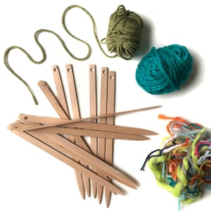 May include: A collection of craft supplies, including wooden weaving tools, skeins of green and teal yarn, and a bundle of colorful yarn scraps. The wooden tools are light brown and have a pointed end.