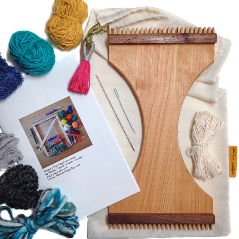 May include: A wooden tapestry weaving companion kit with a light wood frame and dark wood accents. The kit includes yarn in various colors, needles, a pink tassel, and a canvas bag. A printed guide is also included.