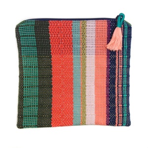Peut inclure: Pochette tiss&eacute;e rectangulaire aux rayures color&eacute;es vertes, rouges, bleues et roses. Elle est orn&eacute;e d'une fermeture &eacute;clair bleu marine et d'un pompon turquoise. Le sac est en tissu textur&eacute;, avec une vari&eacute;t&eacute; de couleurs.