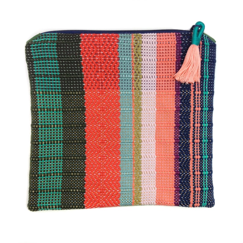 Peut inclure: Pochette tiss&eacute;e rectangulaire aux rayures color&eacute;es vertes, rouges, bleues et roses. Elle est orn&eacute;e d'une fermeture &eacute;clair bleu marine et d'un pompon turquoise. Le sac est en tissu textur&eacute;, avec une vari&eacute;t&eacute; de couleurs.