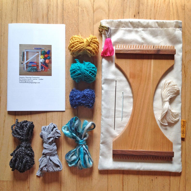 May include: A weaving kit with a wooden loom, yarn in yellow, teal, and blue, and a white canvas bag. The kit includes a booklet with the text "Tapestry Weaving Companion".