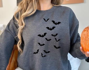 May include: A dark gray sweatshirt featuring a flock of black bats. The bats are arranged in a scattered pattern across the front of the shirt. The sweatshirt is a crew neck style, perfect for Halloween.