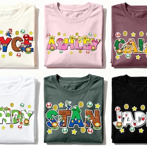 May include: Six folded t-shirts in various colors, each featuring a name in a colorful, video game-themed font. The names are "Bryce", "Ashley", "Caleb", "Sandy", "Stan", and "Jaden", with character graphics and game elements.