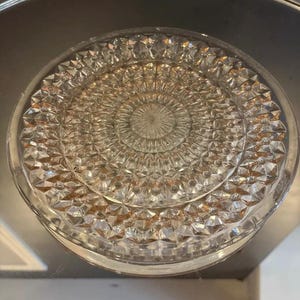 Op de afbeelding: Een heldere glazen plaat met een diamantpatroon. De plaat heeft een verhoogd midden met een kleiner diamantpatroon.