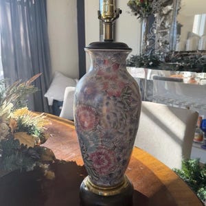May include: A decorative table lamp with a floral pattern. The lamp has a dark wooden base and a brass-colored neck. The body of the lamp is a vase shape with a colorful floral design in pink, blue, and green.