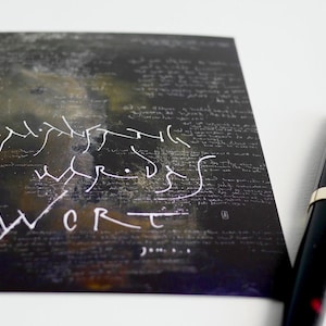 Im Anfang war das Wort, kalligrafische Postkarte mit Bibelvers, wobei das Schriftbild auch die Schöpfungsgeschichte als Hintergrund enthält