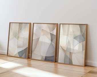 May include: Three framed abstract art prints. Each print features a watercolor design with overlapping shapes in neutral tones of beige, gray, and white. The frames are a light wood color, and the artwork leans against a white wall.