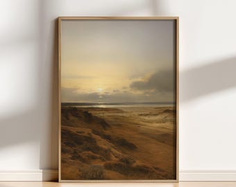 May include: A framed landscape print depicts a coastal scene at sunset. The artwork features a golden sky, a body of water, and a foreground of brown dunes. The print is encased in a light brown wooden frame, adding a touch of warmth to the artwork.