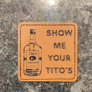 May include: A brown leather coaster with the text "Show Me Your Tito's" and a black and white image of a Tito's Handmade Vodka bottle.