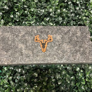 May include: A black silhouette of a deer skull with antlers on a brown leather background.