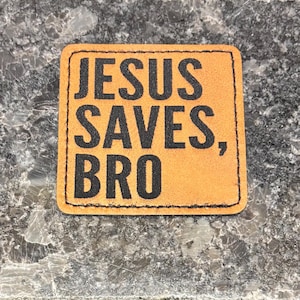 May include: A brown leather patch with black stitching and the text "JESUS SAVES, BRO" printed in black.