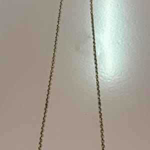 May include: Gold-toned necklace with a delicate chain and a curved pendant. The pendant features a white enamel base with a floral design in red and yellow. A simple and elegant piece of jewelry.