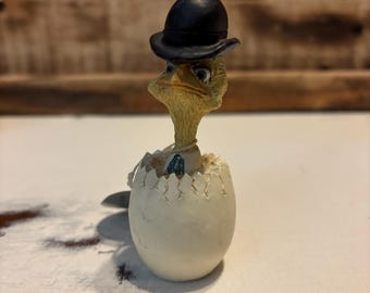 Peut inclure: Un petit oiseau de dessin animé jaune portant un chapeau melon noir est en train d'éclore d'un œuf blanc. L'oiseau a une expression sérieuse sur son visage.