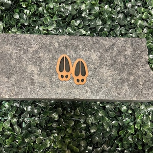 Może przedstawiać: Dwa brązowe odciski kopyt jelenia z czarnymi konturami na szarej powierzchni kamiennej.