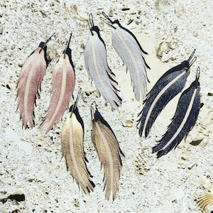 May include: Six pairs of leather earrings in various colors, including silver, gold, black, and pink. Each earring features a feather design with a striped pattern.