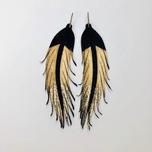 May include: A pair of black and gold leather feather earrings. The feathers are fringed and have a gradient of gold and black.