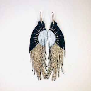 May include: A pair of black leather earrings with gold glitter fringe and white and gold sun designs.
