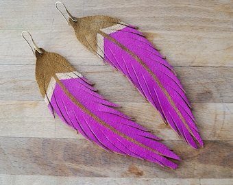 May include: A pair of pink and brown leather feather earrings. The feathers are fringed and have a gold accent.