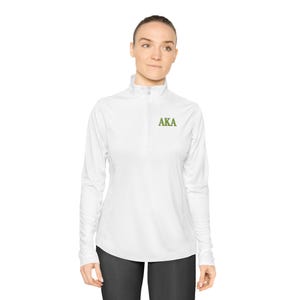 May include: White long-sleeve athletic top with a quarter-zip collar. The letters "AKA" are embroidered in green on the chest. The top is worn with black pants.