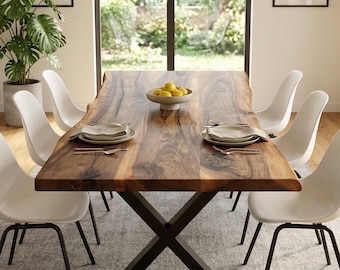 Puede incluir: Un juego de comedor con una gran mesa de madera natural y una base de metal negro en forma de X. Seis sillas blancas con patas negras rodean la mesa. Un cuenco con limones está sobre la mesa. Tres lámparas colgantes cuelgan encima.