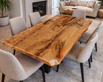 May include: A large, rectangular wooden dining table with a natural edge, showcasing a rich, warm wood grain. The table is approximately 96 inches long and is surrounded by six upholstered chairs with black legs. The setting is a modern dining room.